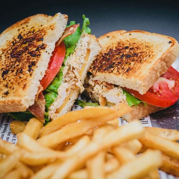 A grilled chicken sandwich with bacon, lettuce, and tomato, served with golden french fries.