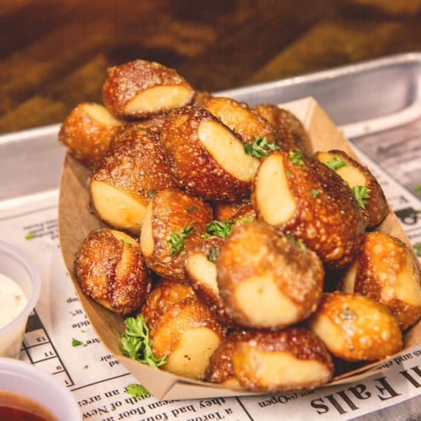 A close-up of golden-brown pretzel bites sprinkled with herbs, served in a paper tray.