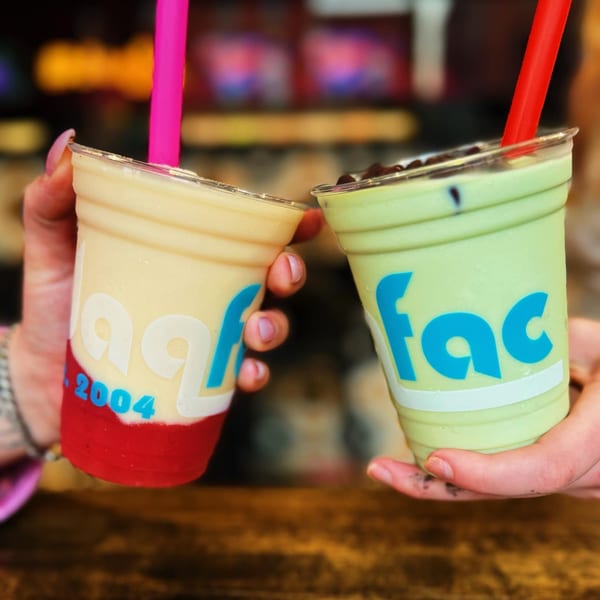 Two hands holding up plastic cups of Daiquiri Factory's frozen drinks, one strawberry and one green.